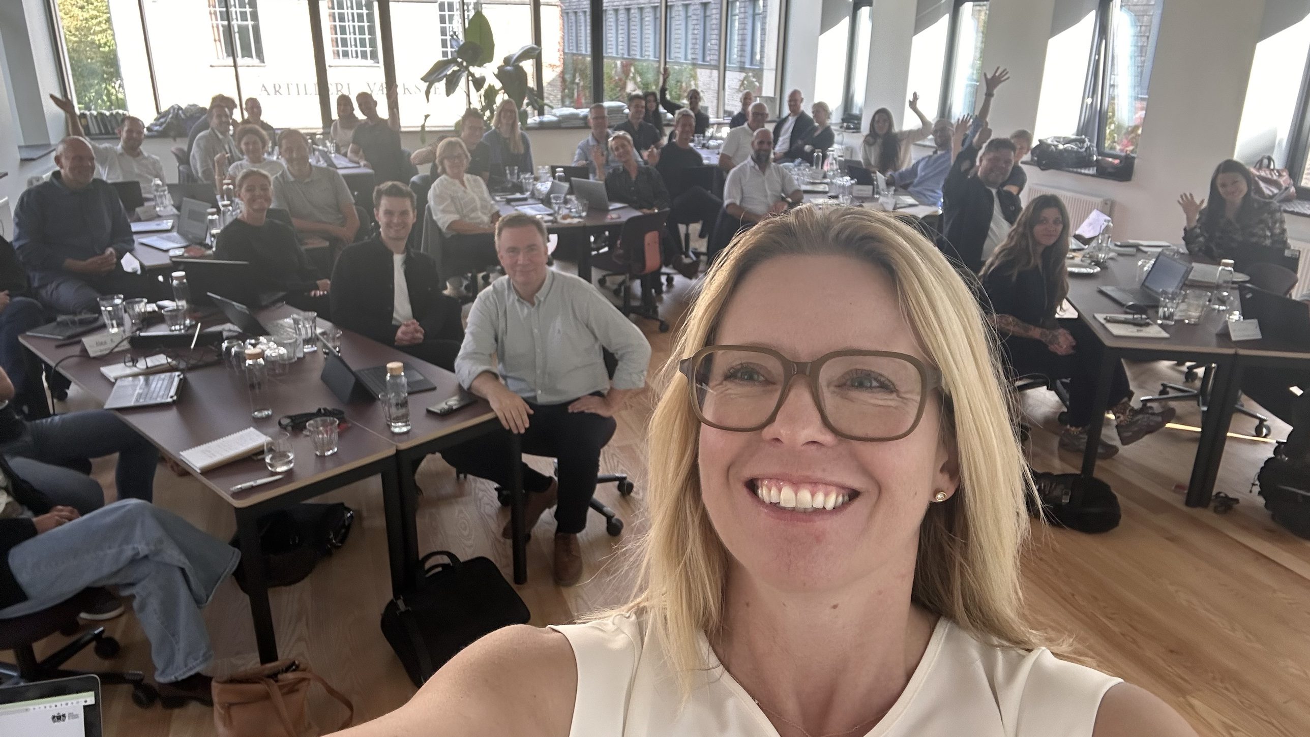 Loa Brix tager en selfie foran et fyldt undervisningslokale med kursister, der vinker