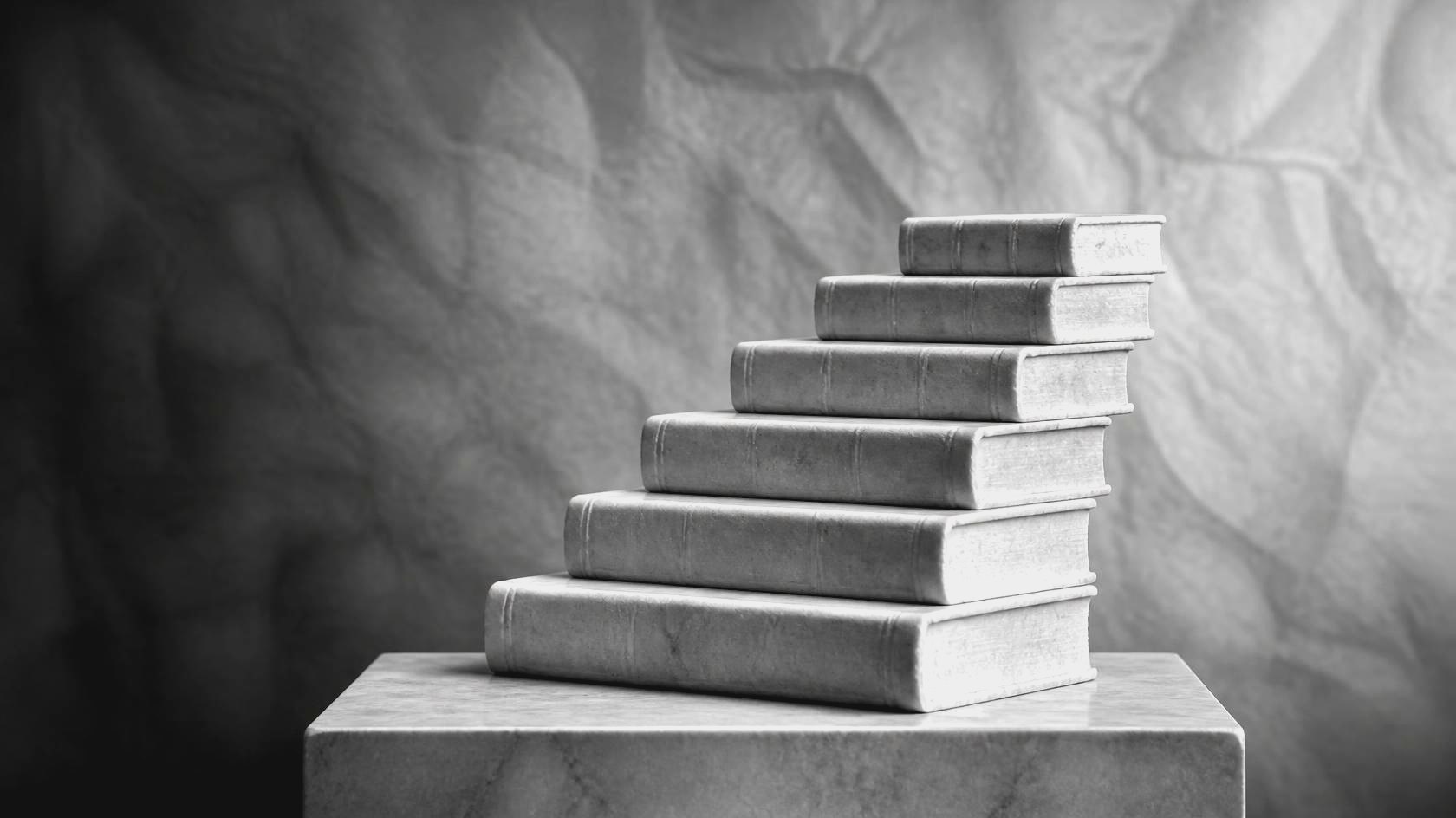 Six books carved in marble stacked as steps on a plinth in front of crumpled paper – the steps of learning